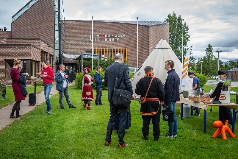Gruppe mennesker st&aring;r spredt rundt p&aring; plenen utenfor campus Alta