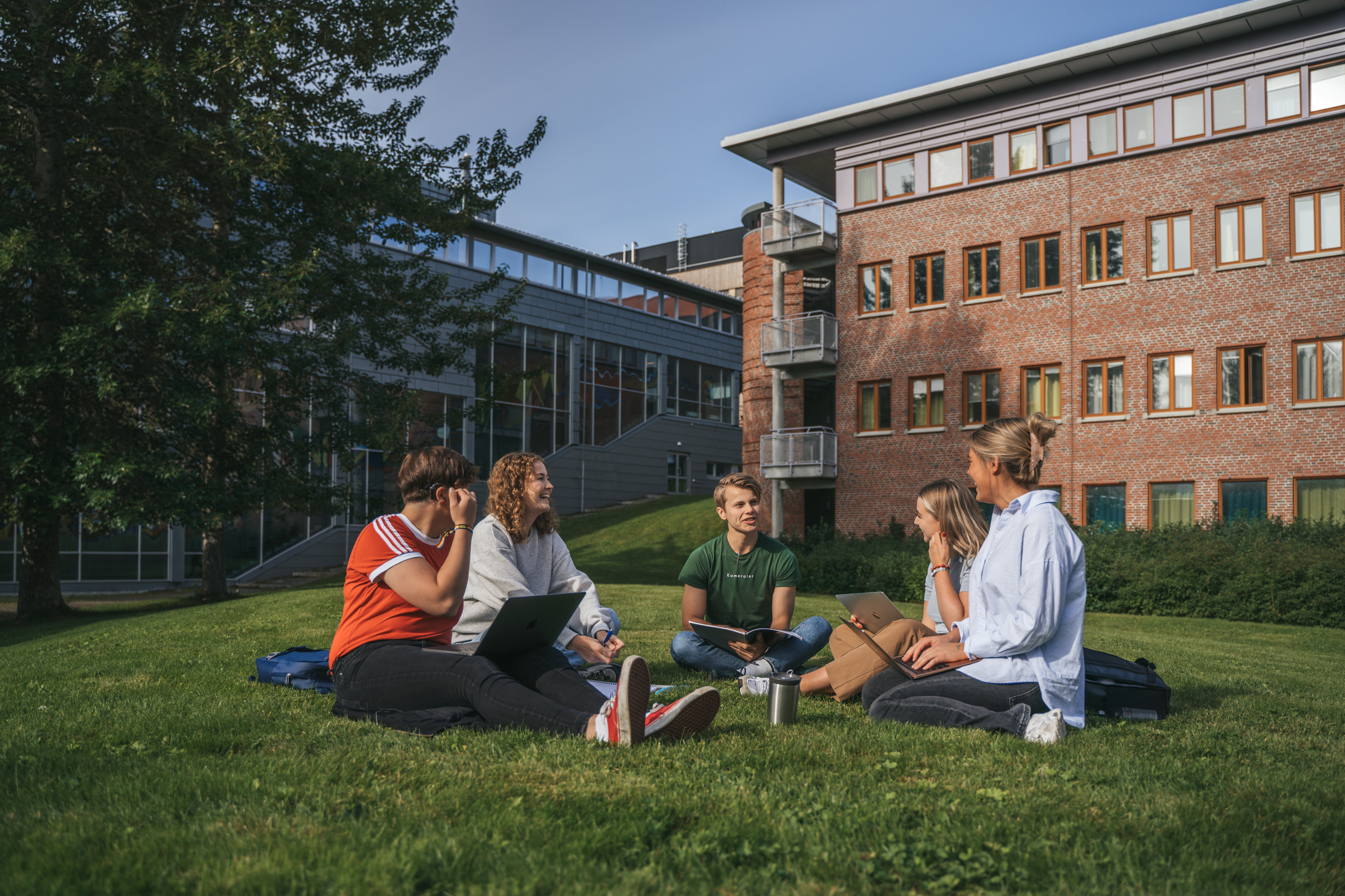Studenter sitter i sirkel og smiler p&aring; plen