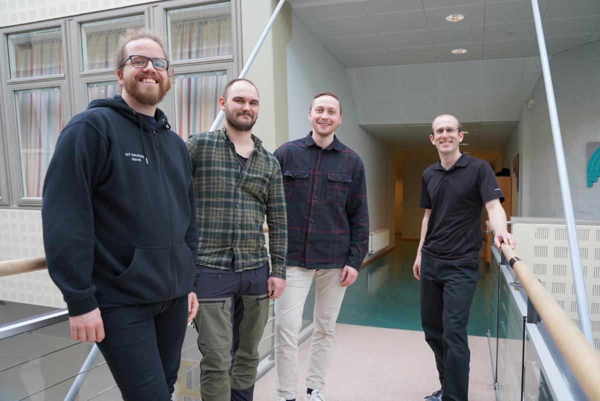 Fire personer smiler til kamera fra en gangbru p&aring; UiT i Narvik