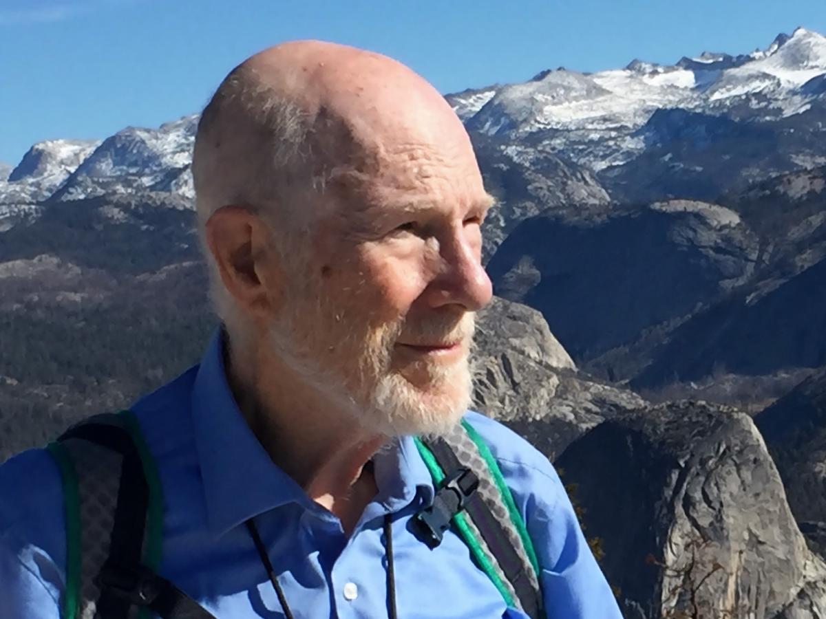 Portrett av en eldre mann i pent v&aelig;r. I bakgrunnen en dramatisk fjellkjede.