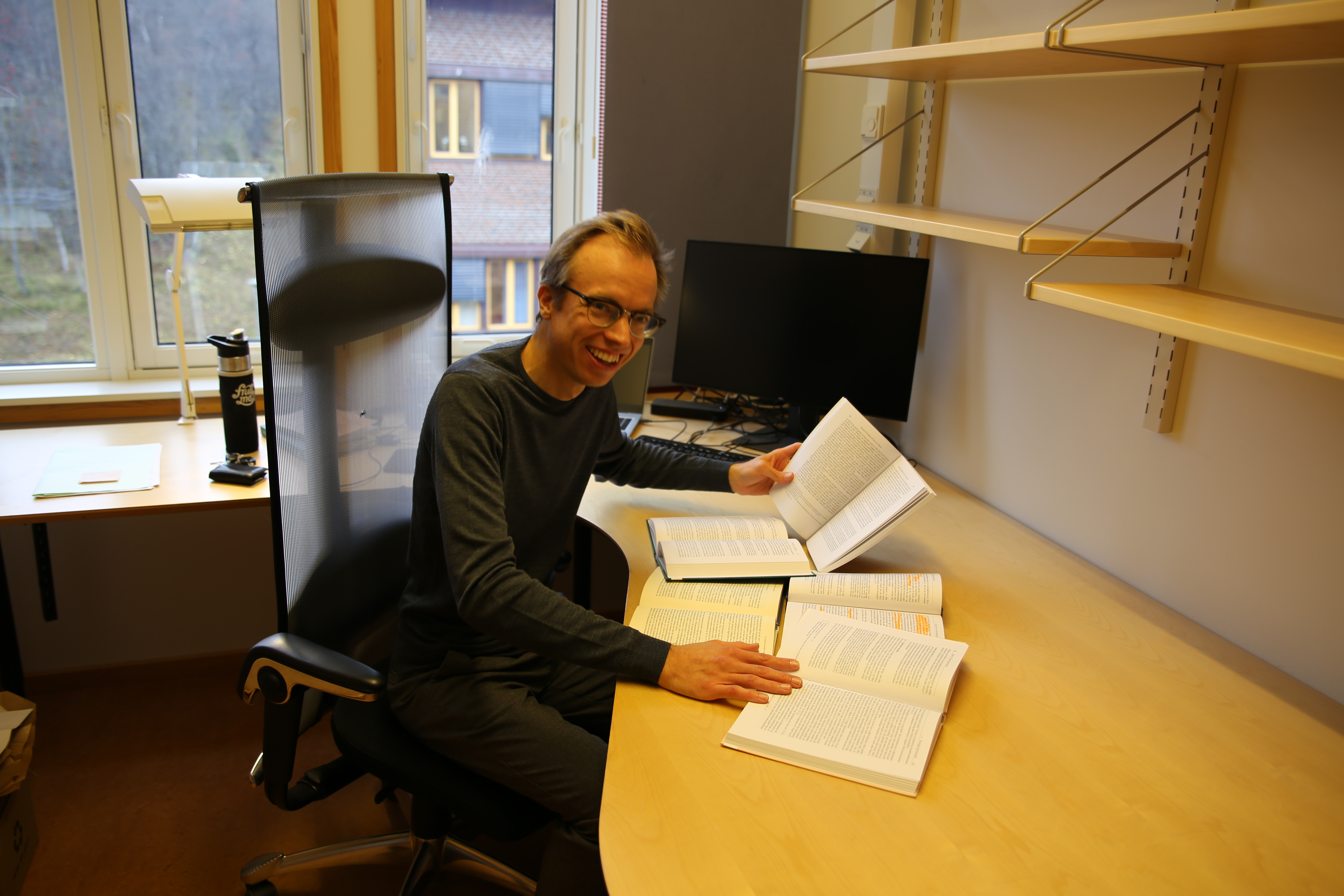 Sondre smiler og poserer p&aring; et ganske tomt kontor med et par b&oslash;ker. 