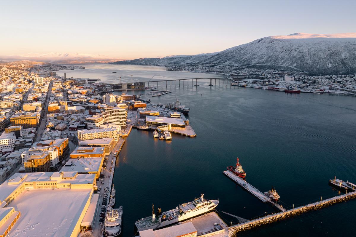 foto fr&aring; luften av en sn&oslash;dekka by ved eit sund. fjell og sj&oslash; mot horisonten.