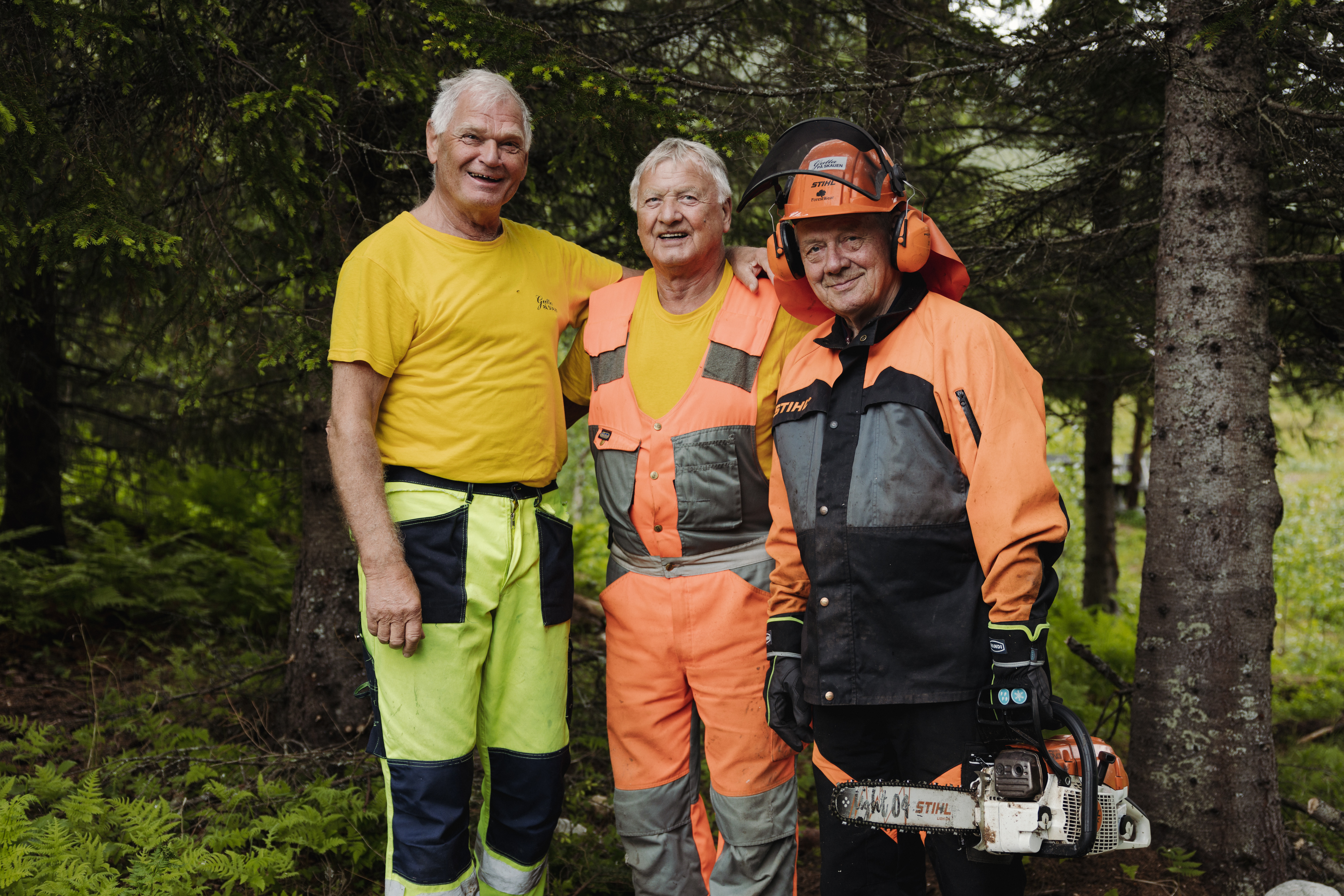 tre eldre menn som jobber i skogen med arbeidskl&aelig;r og motorsag