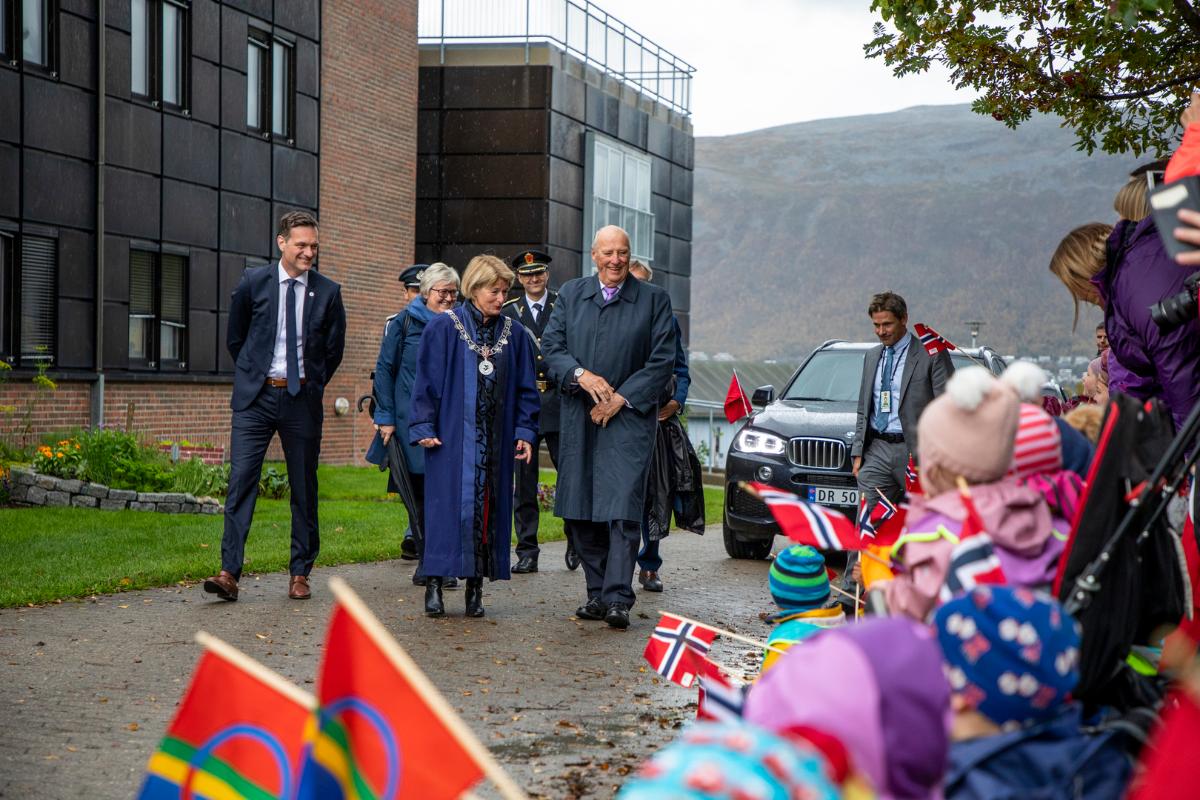 Kong Harald besøker UiT 2018.jpg En gruppe mennesker går på en gangsti, barn med flagg langs stien.